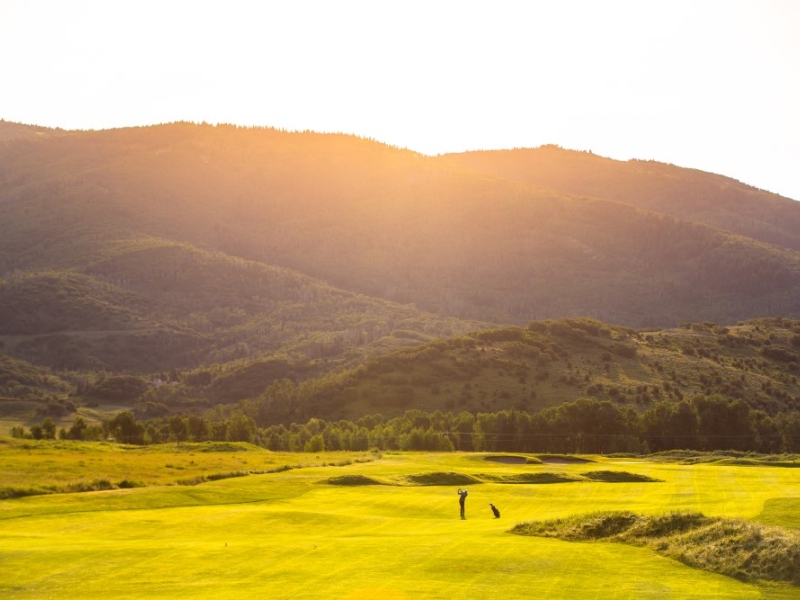 Golfer hitting at sunrise with mountains in background
